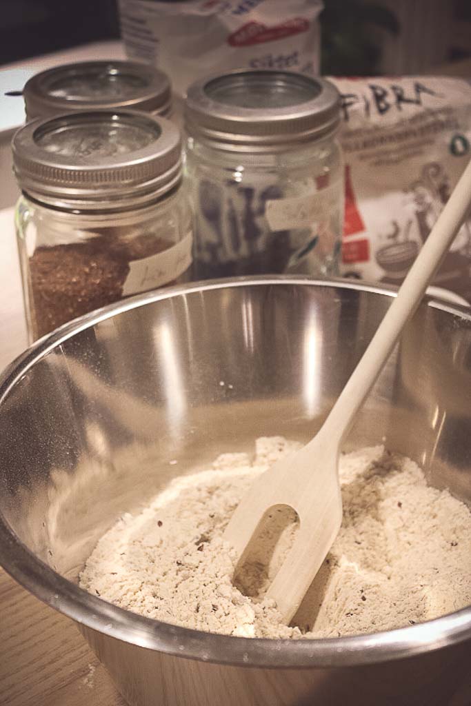 bakebolle med melblanding. Fullkornsmelpose, hvetemelspose og krukker med frø i bakgrunnen