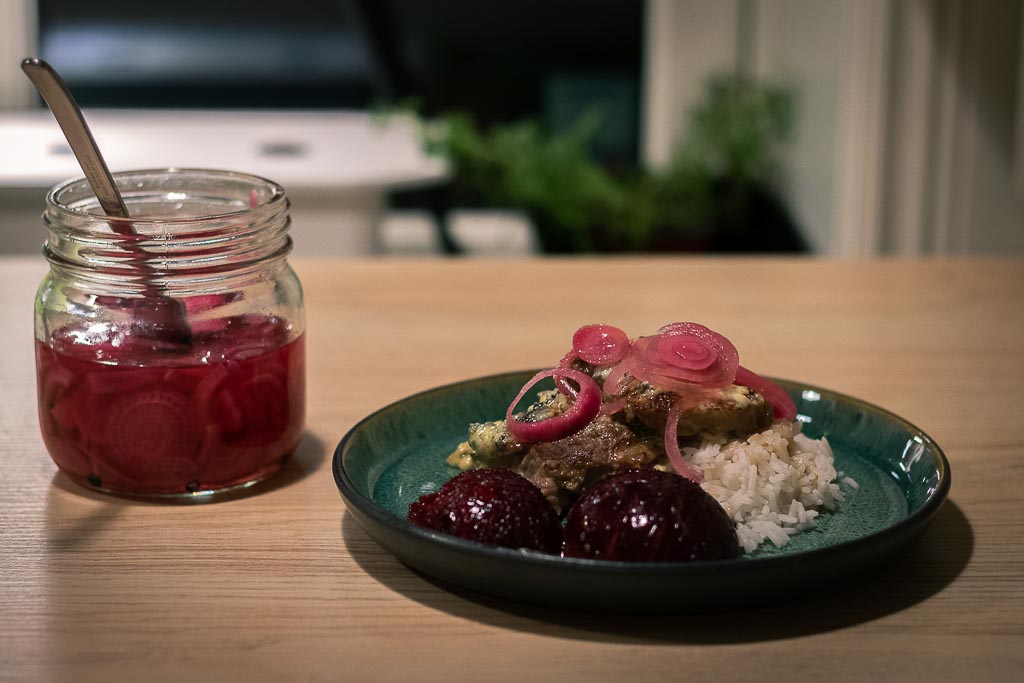 Nakkekotelett med plommer og blåmuggeostsaus toppet med sylta rødløk på en tallerken.