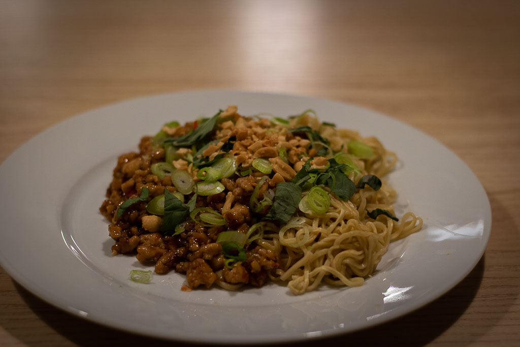 Hvit tallerken med nudler med kyllingkjøttdeig,  toppet med peanøtter, vårløk og koriander.