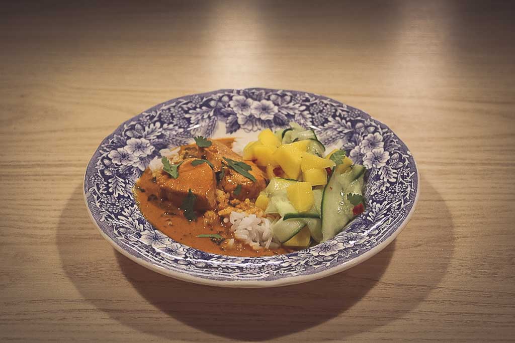 Dyp tallerken med kyllingbiter i currysaus med mango og agurksalat