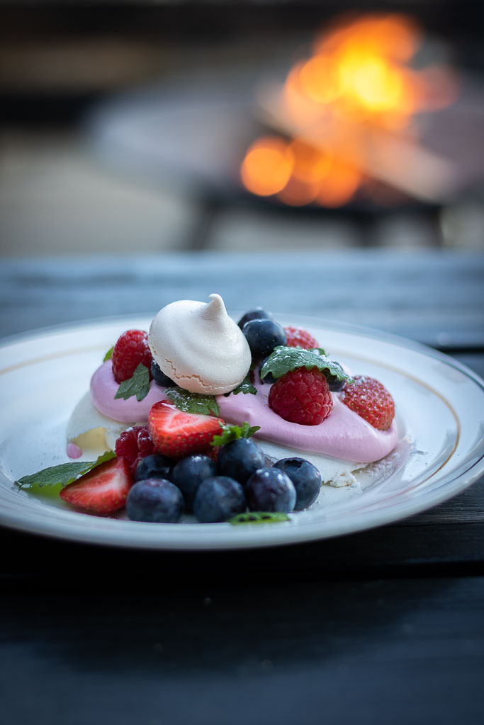 pavlova med masse friske bær, rosa krem, sitronmelisse og et glass sprudlende ved siden av