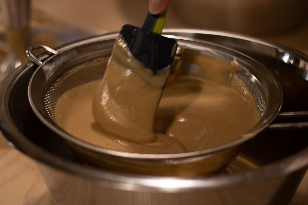 Pepperkakeisrøra blir silt gjennom en sil i en bolle med slikkepott som redskap.