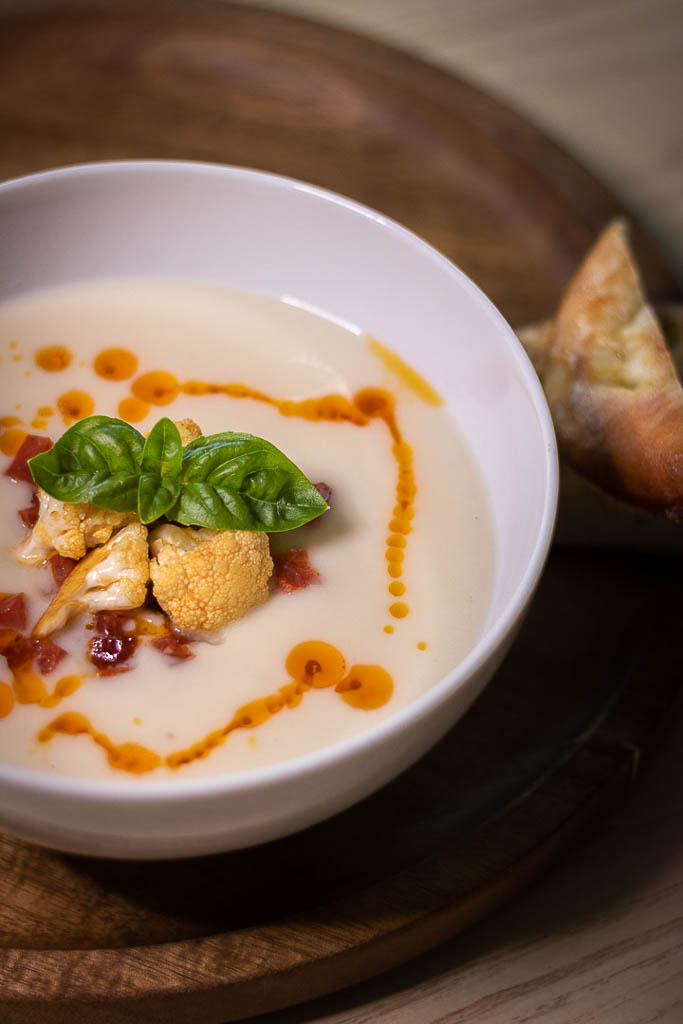 Blomkålsuppe i dyp skål med brød ved siden av