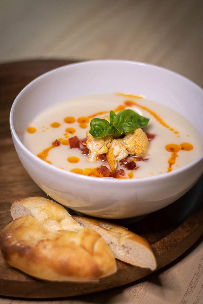 Blomkålsuppe i dyp skål med brød ved siden av