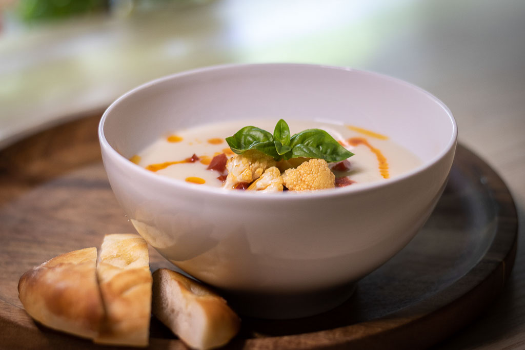 Blomkålsuppe i dyp skål med brød ved siden av