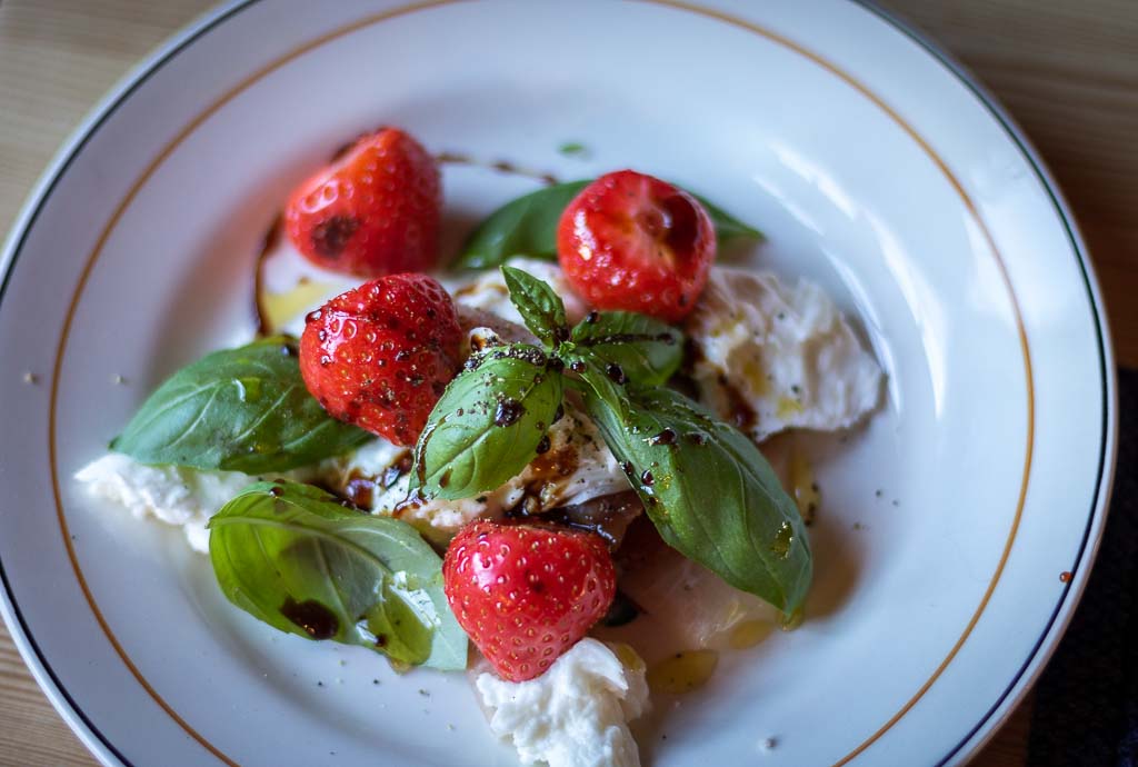 jordbær og mozzarella med spekeskinke, basilikum og oljer på en tallerken