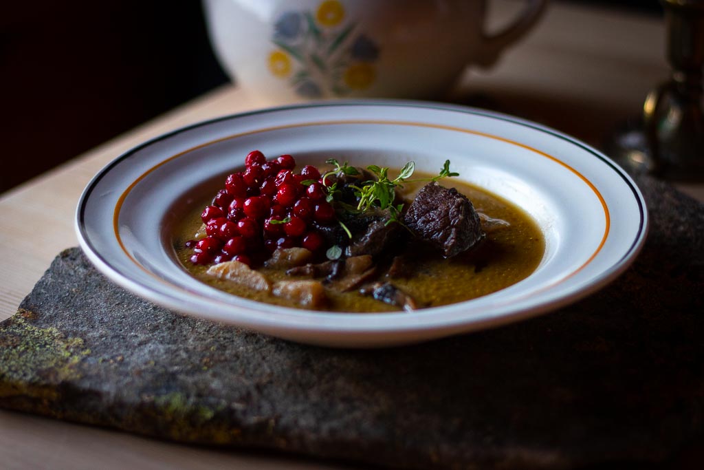 viltgryte i dyp tallerken med tyttebær, stående på en stein